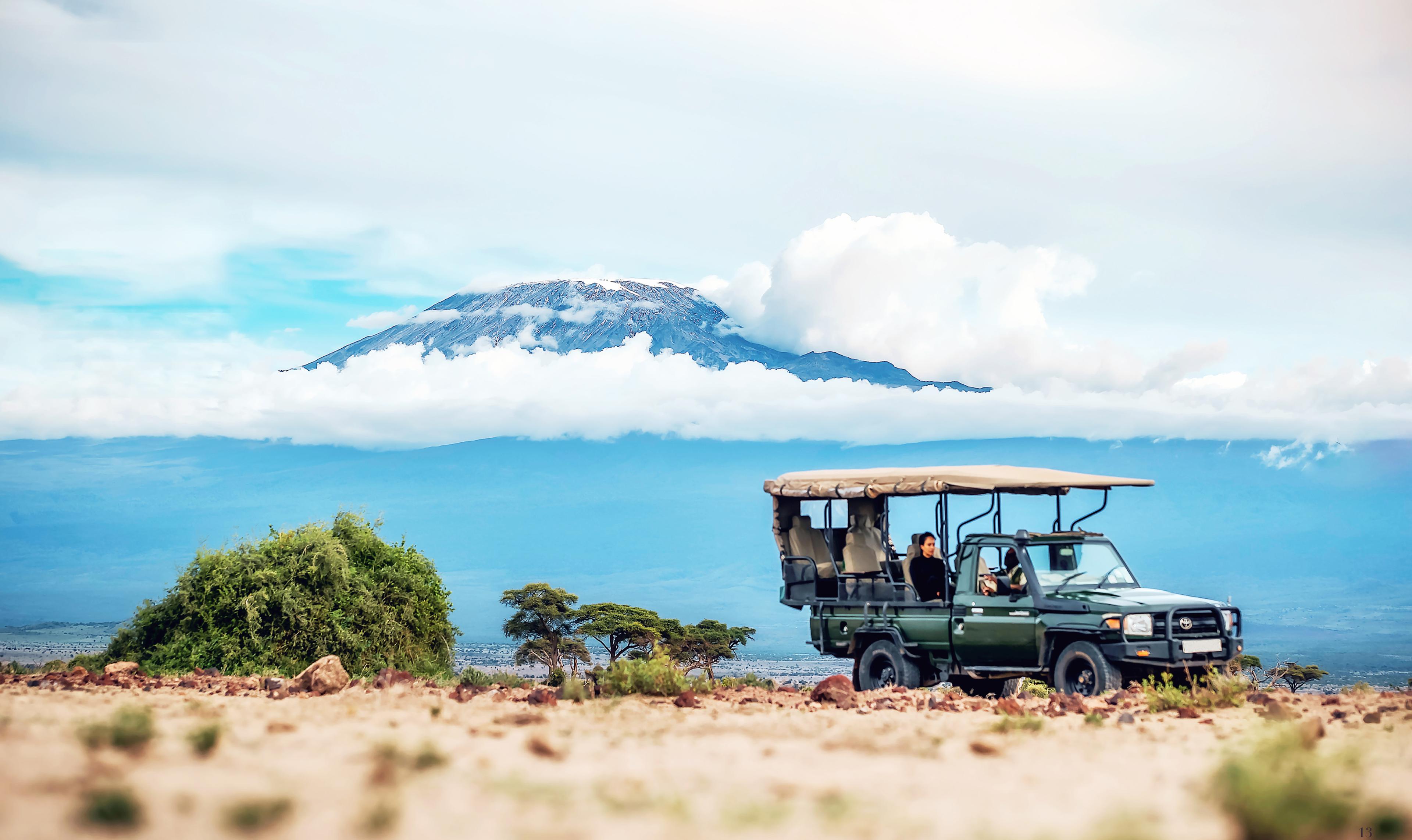 Safari vehicle on the plains with a mountain rising above the clouds